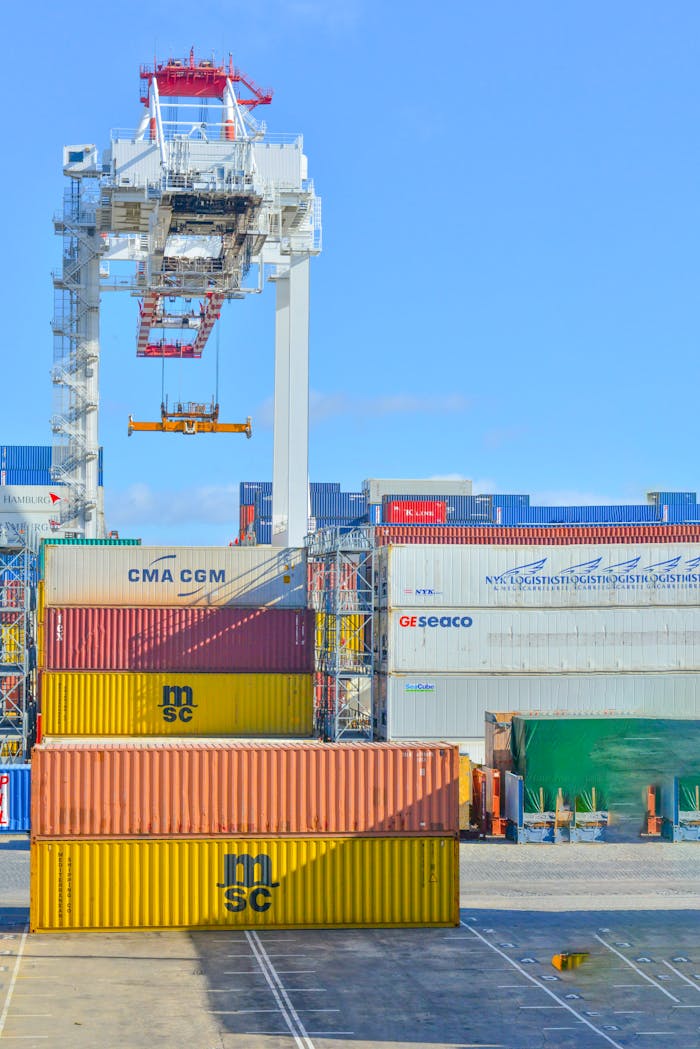 why-choose-us Stacked cargo containers in a sunny port industrial setting with crane.