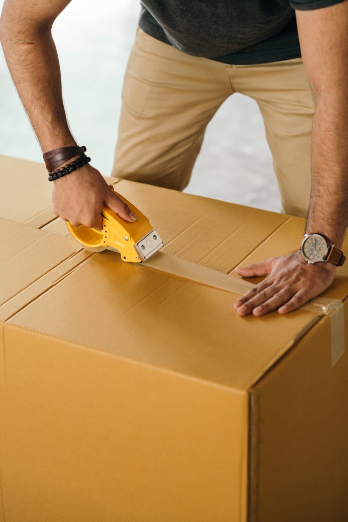 portfolio-03 Unrecognizable man sealing box with duck tape while preparing for moving out